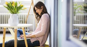 Smiling woman sitting on floor next to table with tulips using laptop