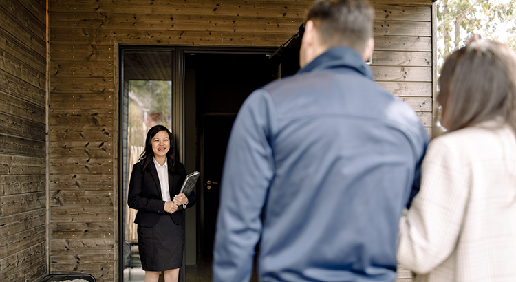 Smiling real estate agent greeting couple at entrance of house