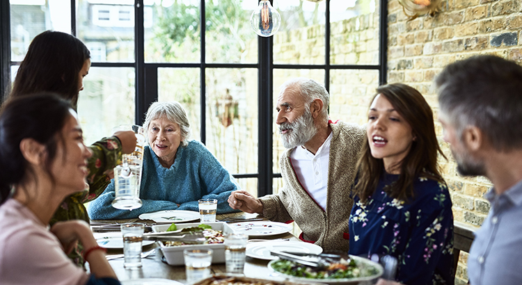 Mixed age ranges enjoying meal together in family home, pre teen girl pouring water for dinner guests, social vibrant lively family gathering